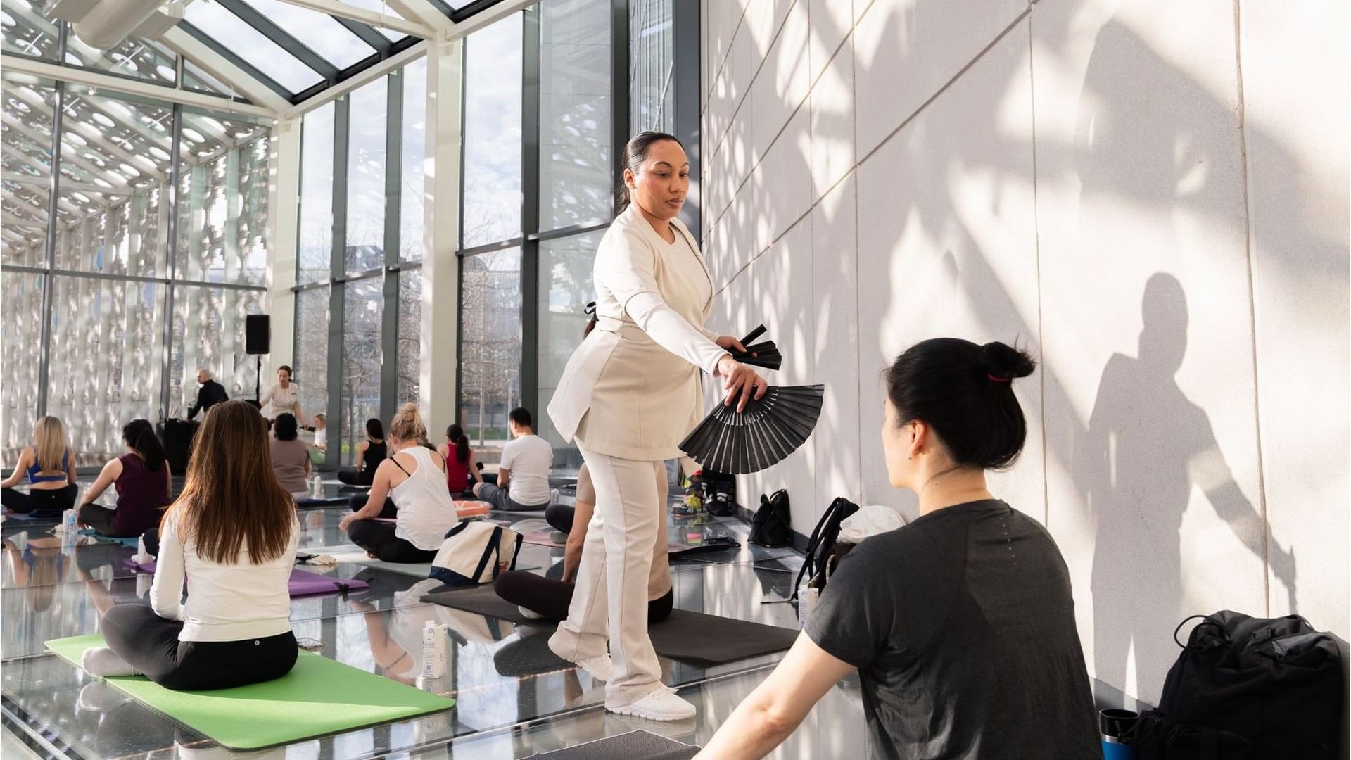 Wellness specialist using a folding fan beside seated guests during a guided group relaxation session at Hotel X Toronto