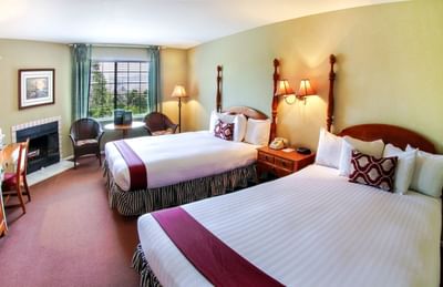 Two queen beds in hotel room with fire place and window view