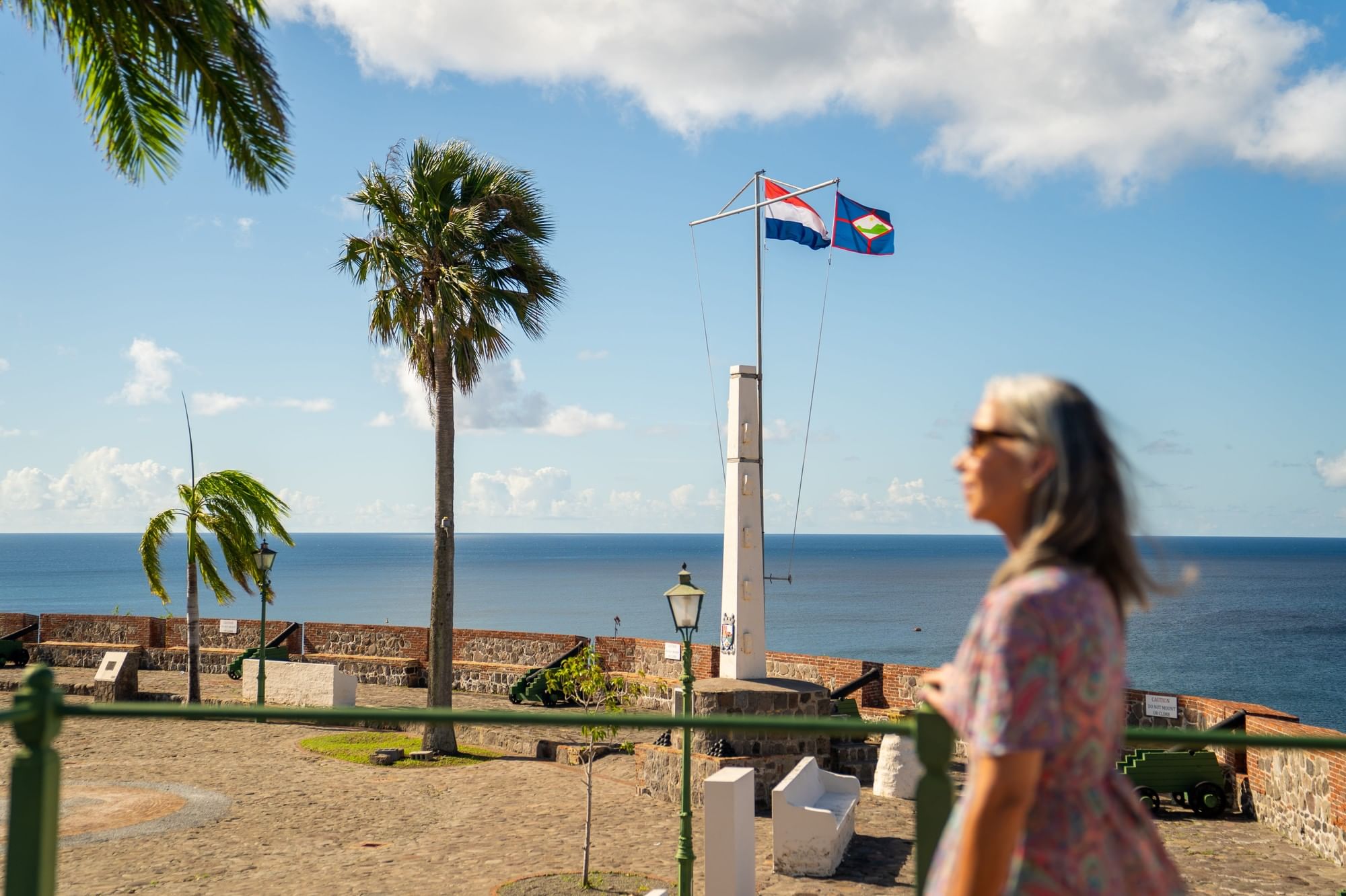 Visitor at Fort Oranje in St. Eustatius looking toward the flagpole monument, cannons and the Caribbean Sea