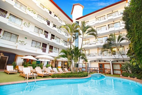 Sunny courtyard swimming pool with lounge chairs and white umbrellas by multi-story balconies at Casa Dona Susana