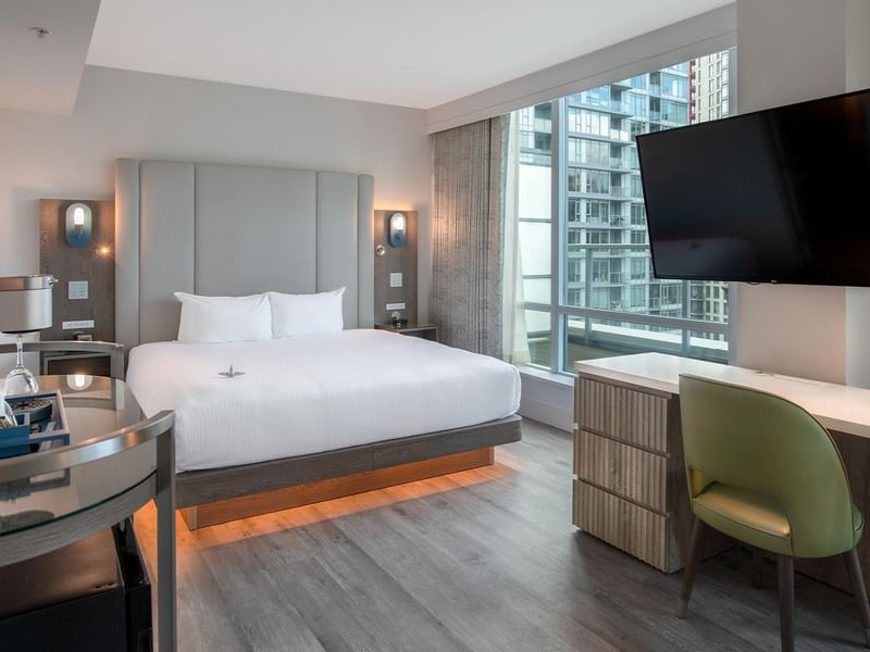 Hotel room with large bed, desk, TV, and large windows.