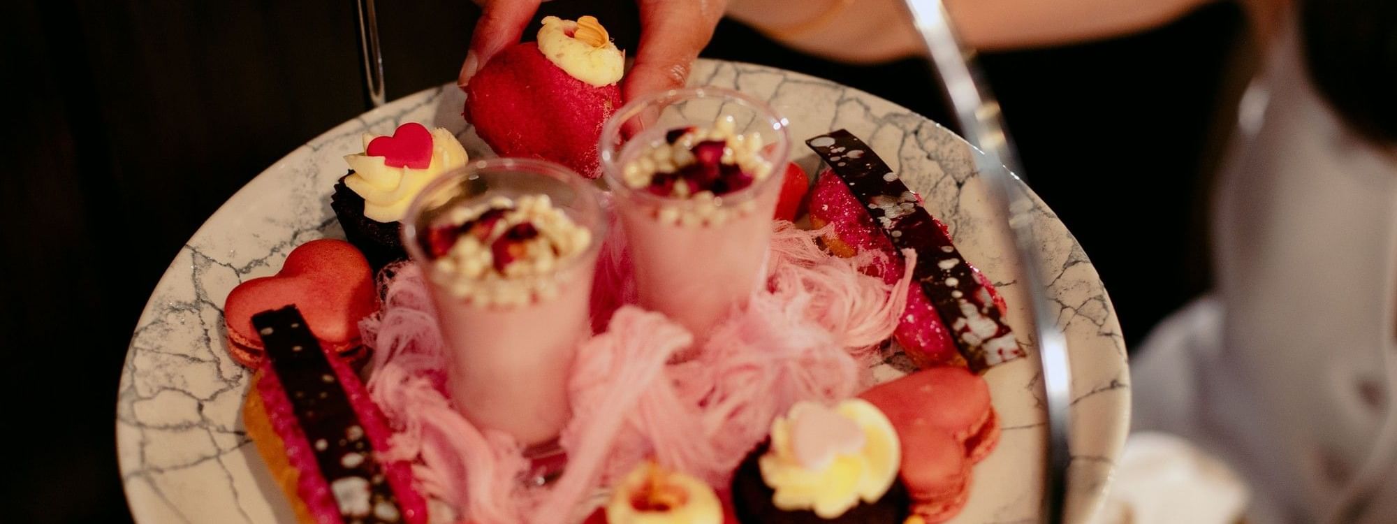 Woman picking a strawberry tart from a three-tier dessert platter for Mother's Day High Tea.