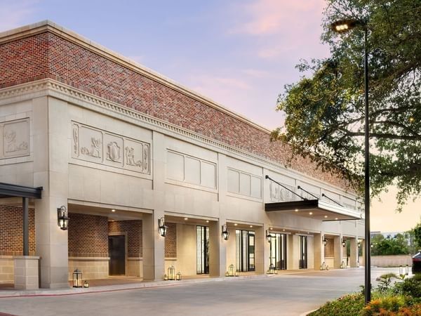 Exterior view of Warwick Melrose Dallas by lanterns under a sunset sky surrounding the grand Entrance