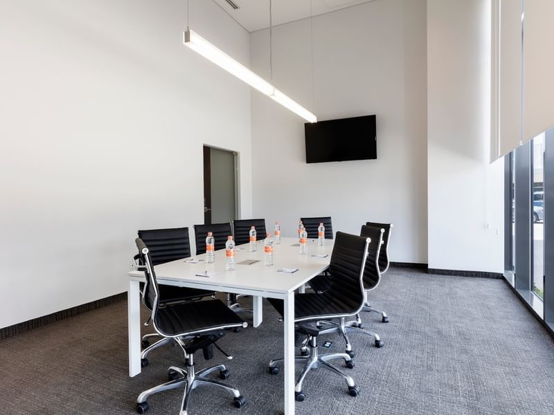 Modern Cancun meeting space at Fiesta Inn Express Cancún Cumbres with a white table, leather chairs, and a TV