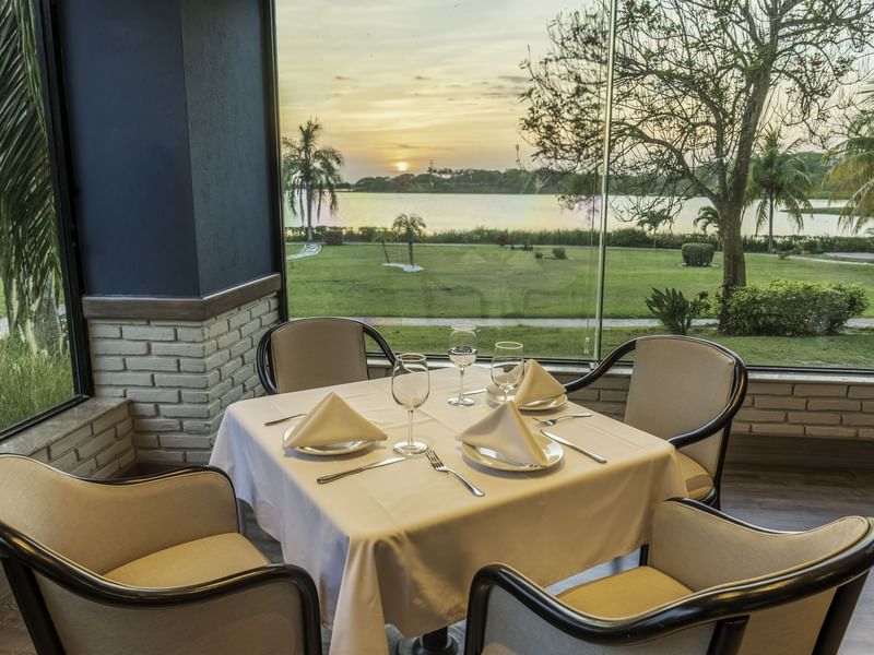 Set dining table by spacious windows, offering view of lake in sunset surrounded by lush greenery at Fiesta Inn