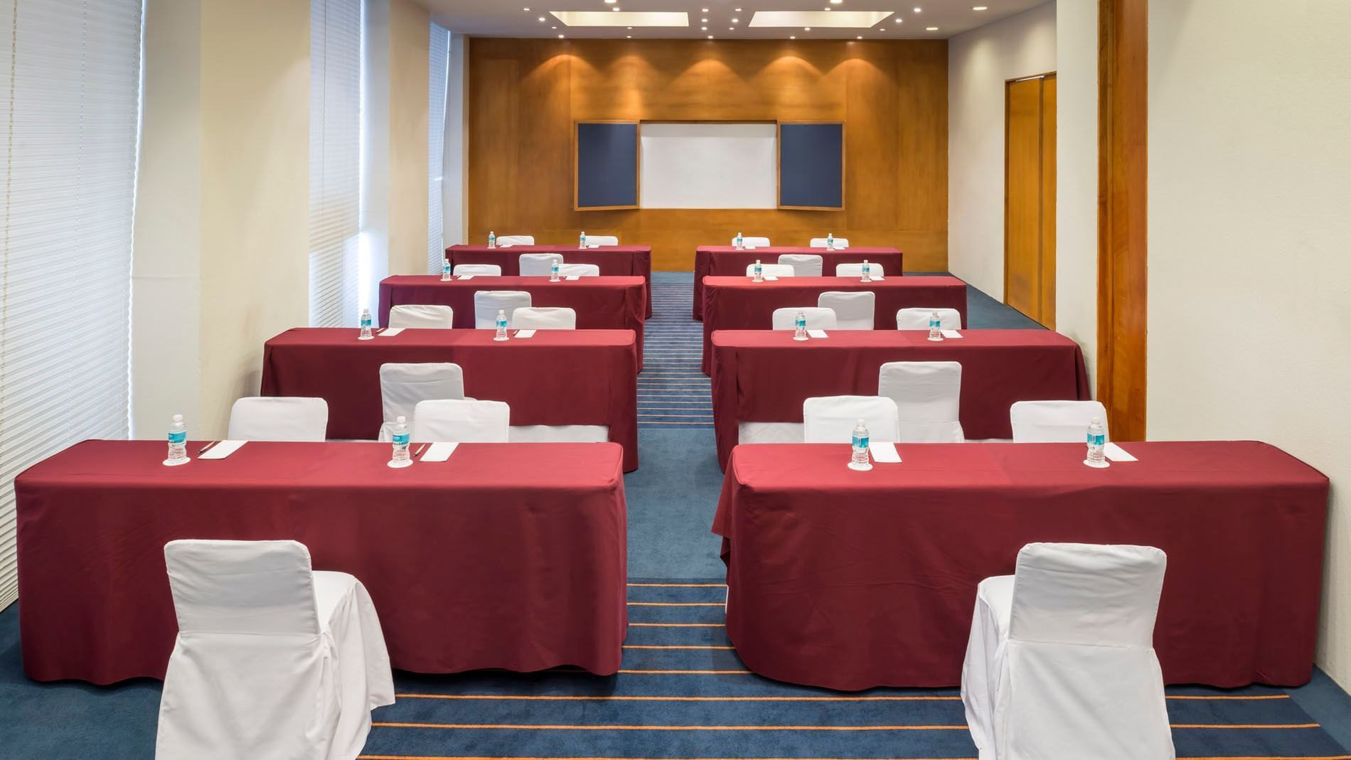 Classroom set-up with a projector screen and carpeted floors in the Dubai Venue at Real Inn San Luis Potosi