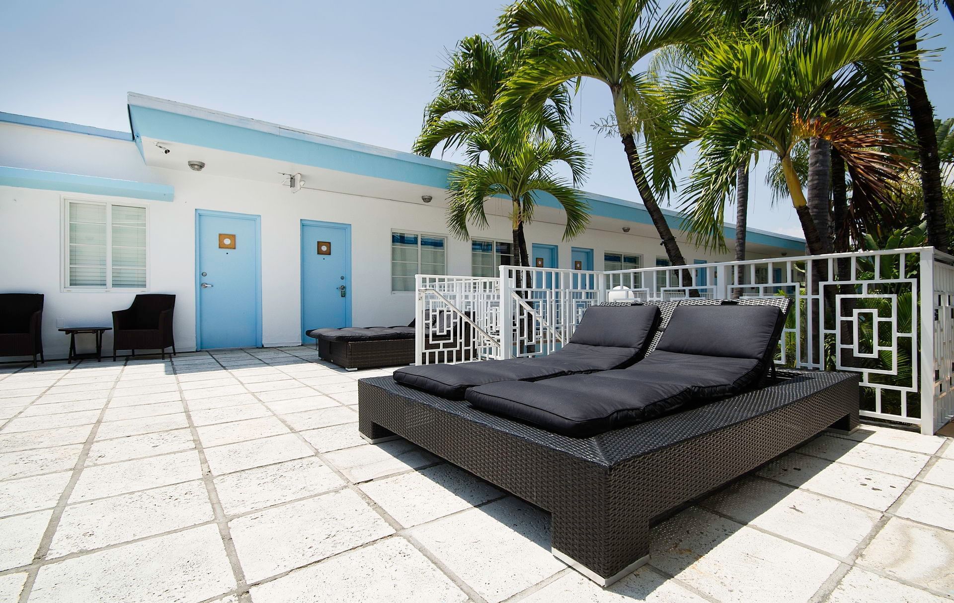 A white building with blue trim and palm trees, with lounge chairs on a patio.