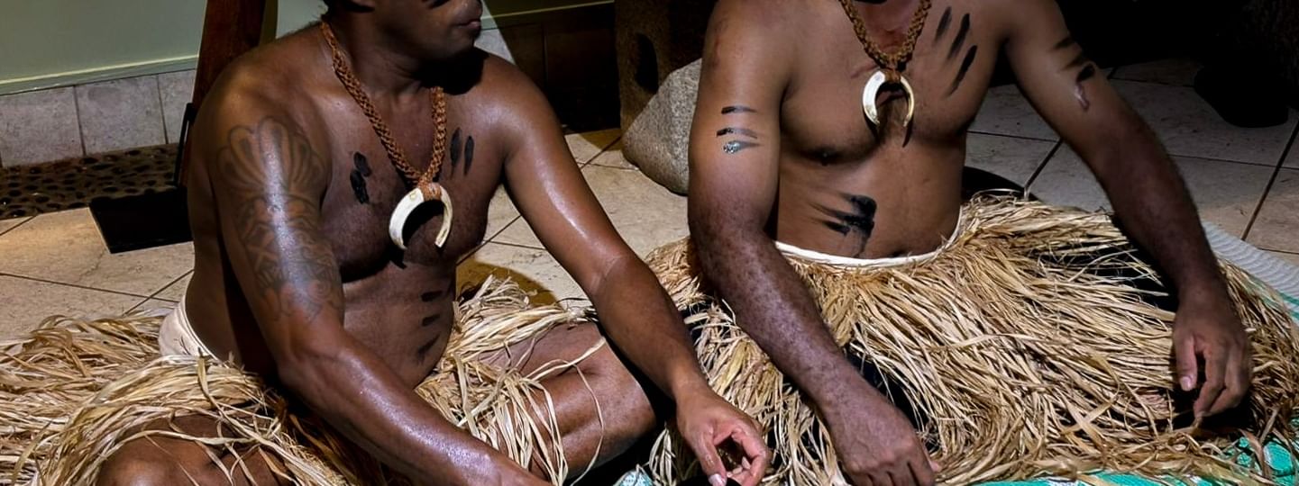 Two men in traditional attire preparing cultural items on the floor at Warwick Fiji Resort and Spa, Korolevu