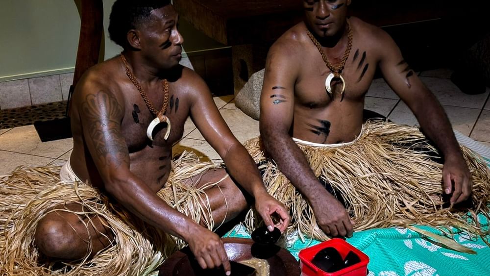 Two men in traditional attire preparing cultural items on the floor at Warwick Fiji Resort and Spa, Korolevu.
