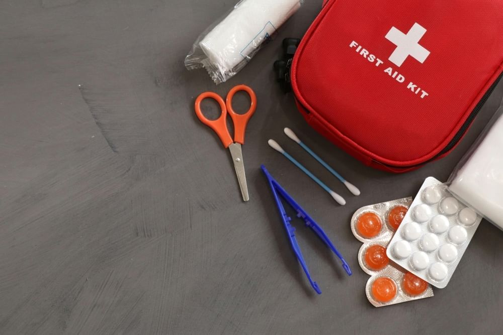 A red first aid kit surrounded by supplies like tablets, tweezers, scissors, and q-tips. 