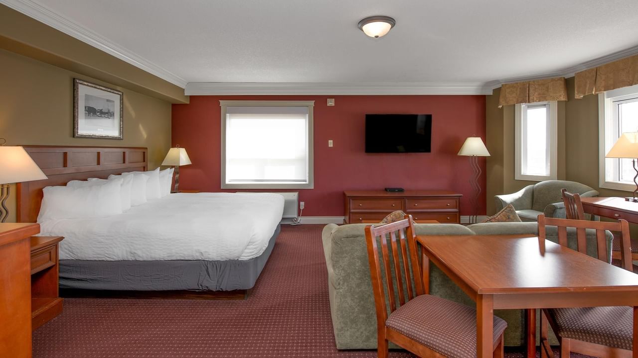 Spacious hotel suite with king bed, dining area, sofa, wall-mounted TV, and red accent wall at Coast Edson Hotel.