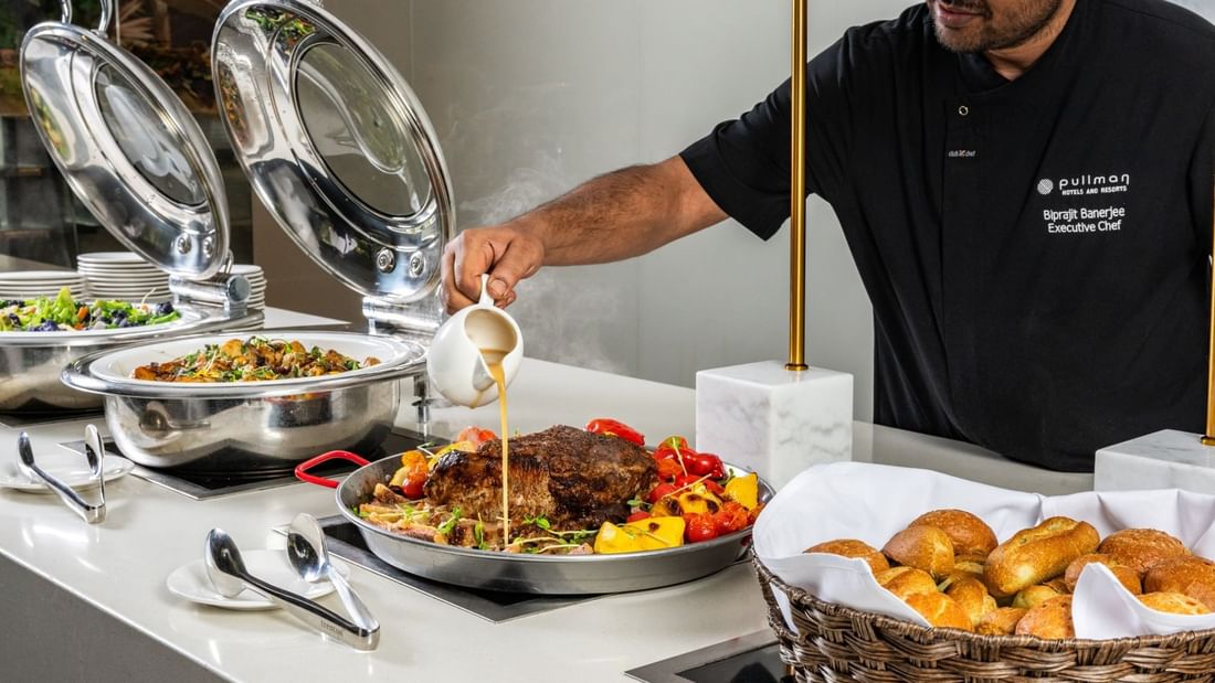 Chef pouring gravy into meat dish in a restaurant at Pullman Sydney Hyde Park