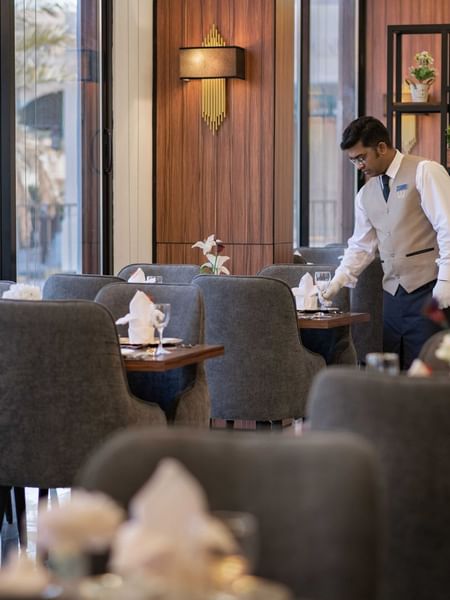 Waiter setting a table with glassware and napkins by a black metal room divider at Warwick Al Jubail