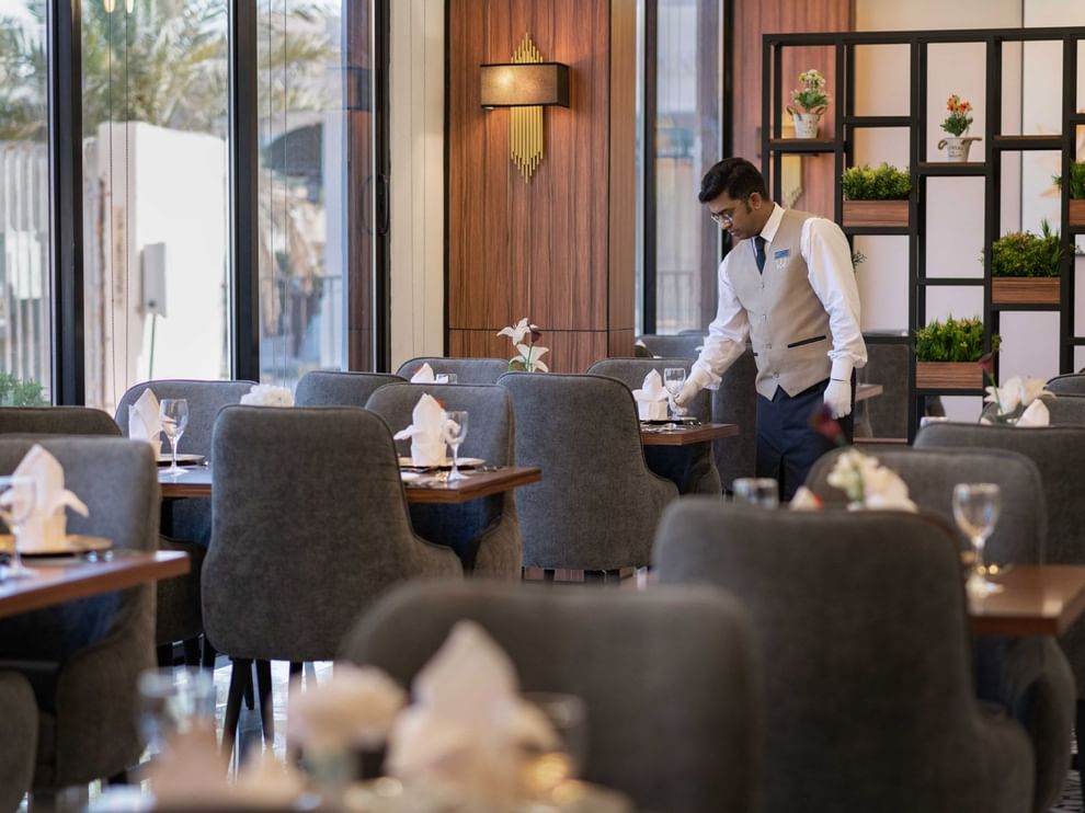 Waiter setting a table with glassware and napkins by a black metal room divider at Warwick Al Jubail