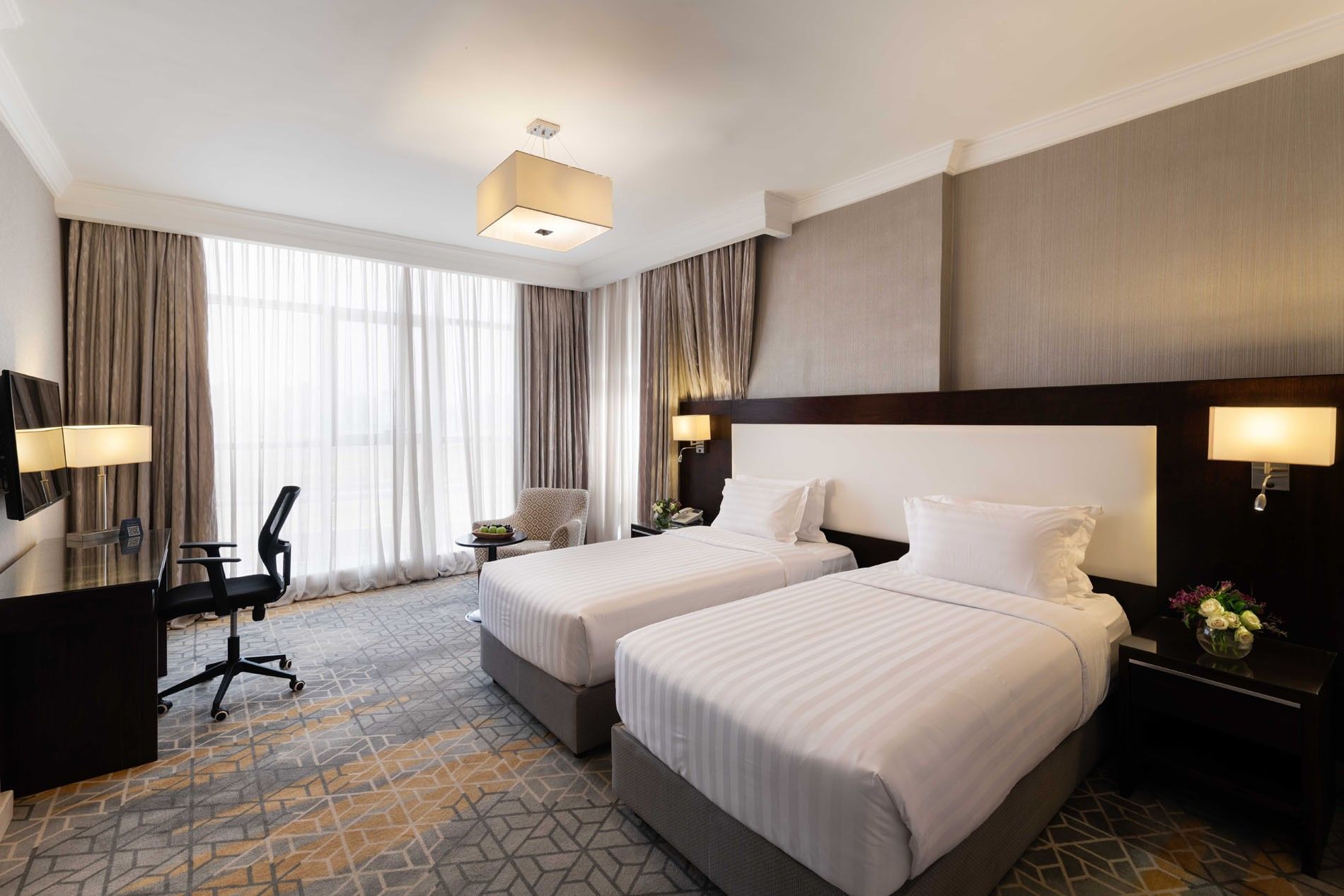 Work desk, nightstand, and cozy lounge chair by the beds in the Deluxe Room at Warwick Hotel Jeddah