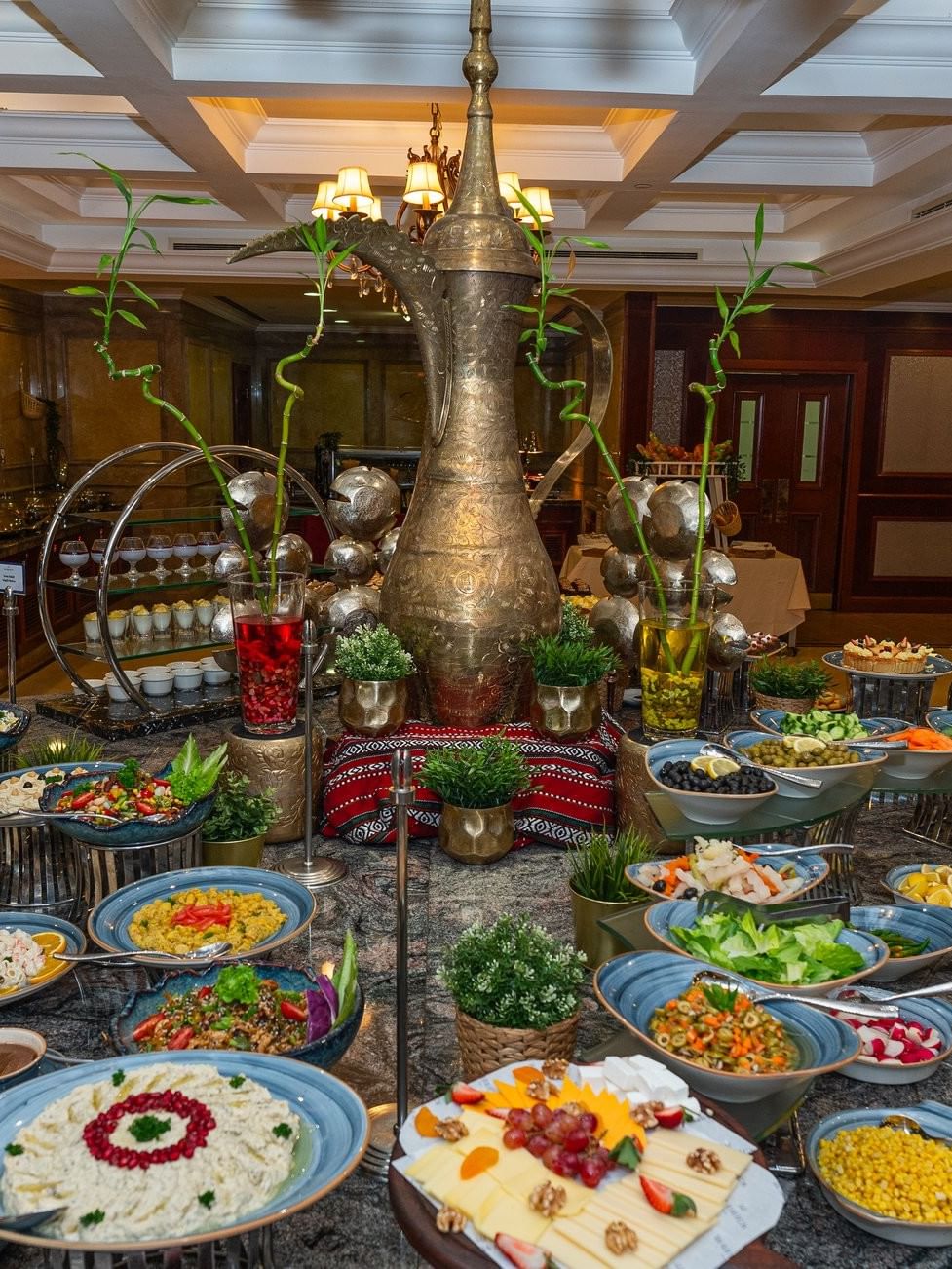 Gourmet salads in blue bowls by a large brass pitcher under a coffered ceiling in L’auberge at Warwick Doha Hotel