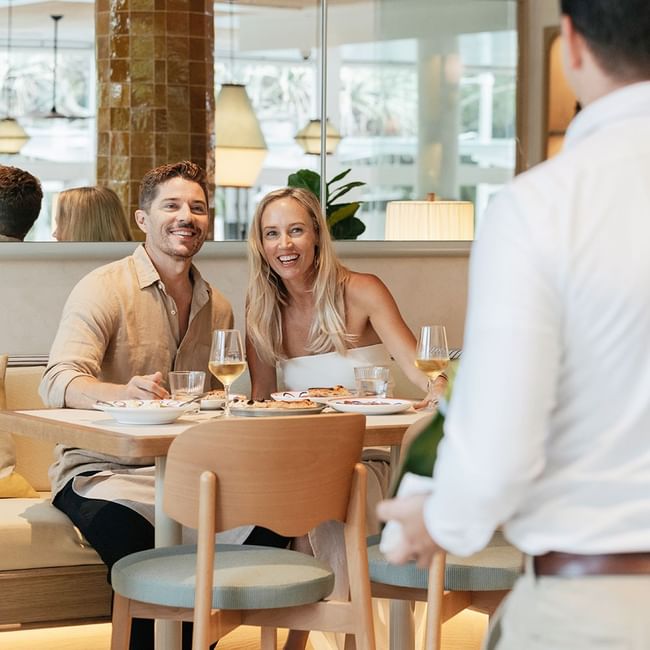 A couple dining at Elysium Hotels with a waiter presenting a wine bottle