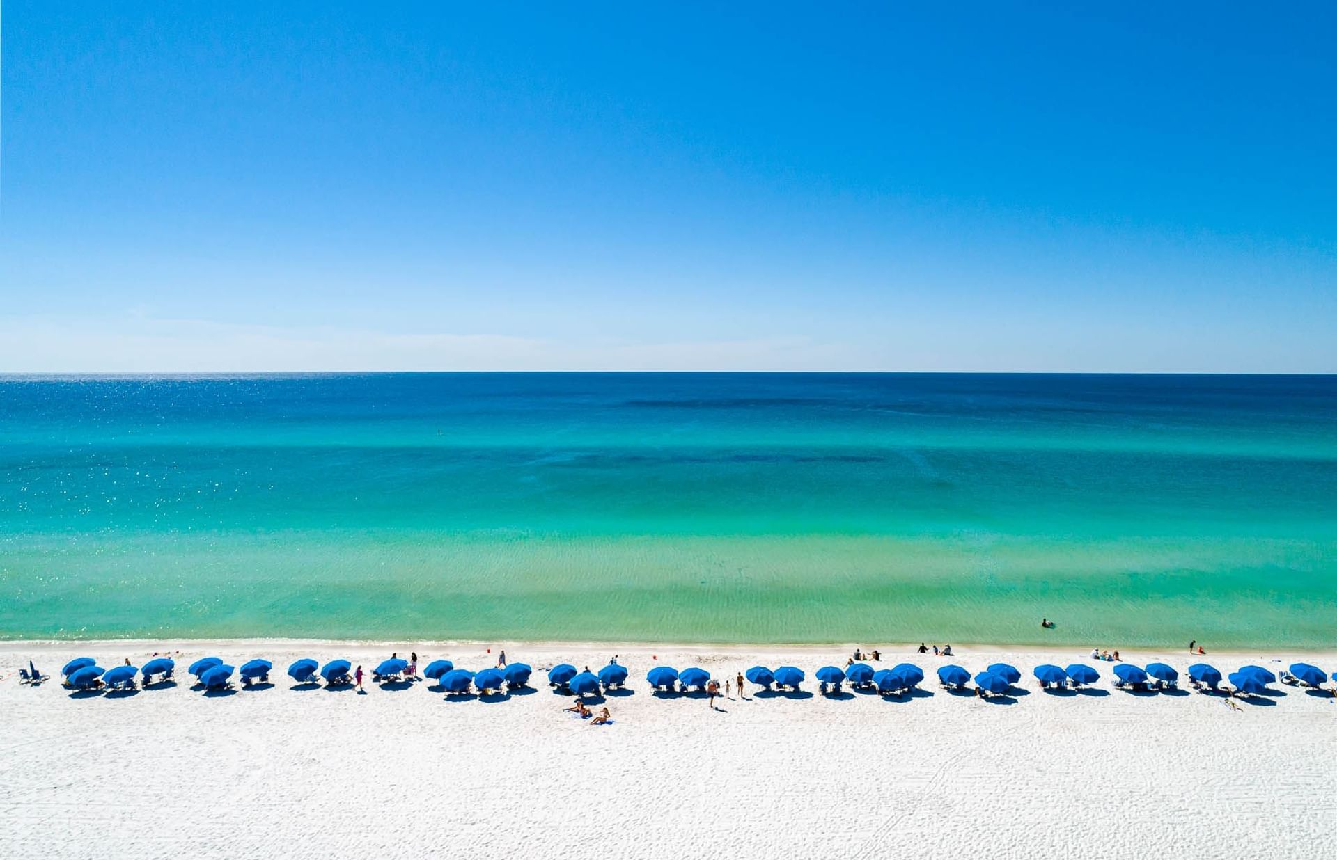 Distant view of sunbeds & umbrellas lined by the Sea on a sunny day at Watersound Inn