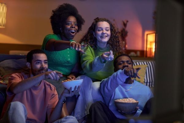 Surprised group of friends watching a movie together and pointing at a TV together in a dark living room.