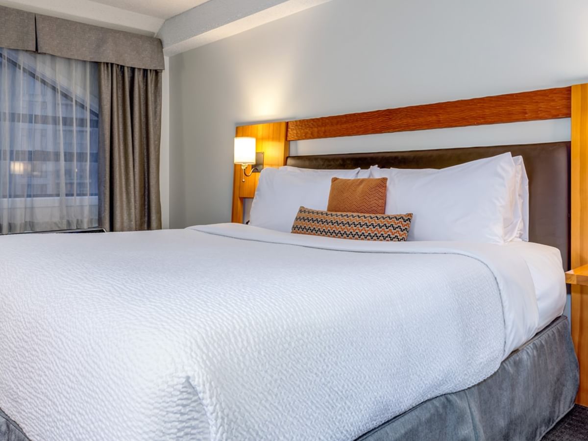 A hotel room with a large bed, white bedding, two pillows, and a wooden headboard with lamps.