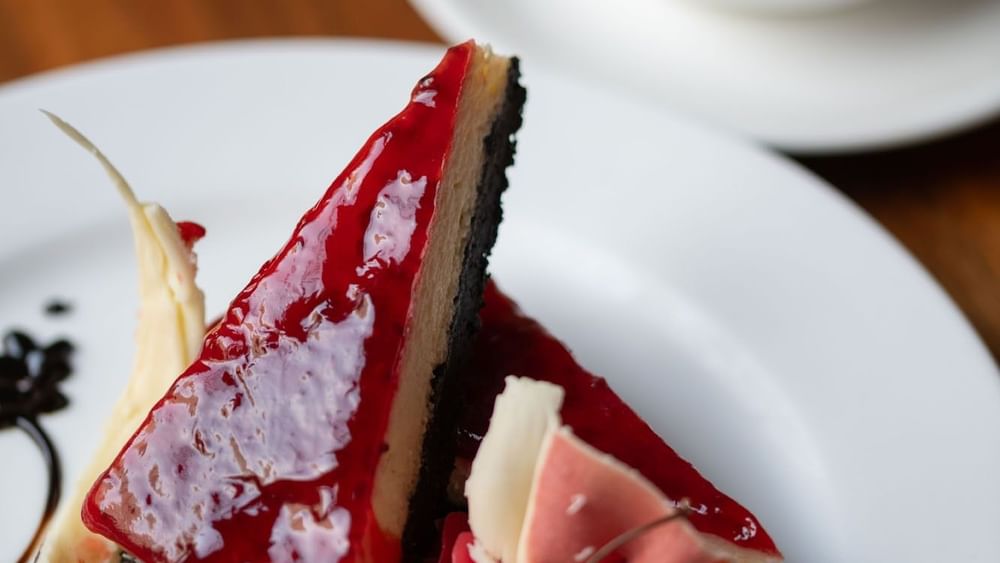 Two slices of cheesecake with a red glaze and dark crust served in the Artist Lobby Lounge at Warwick Hotel Jeddah