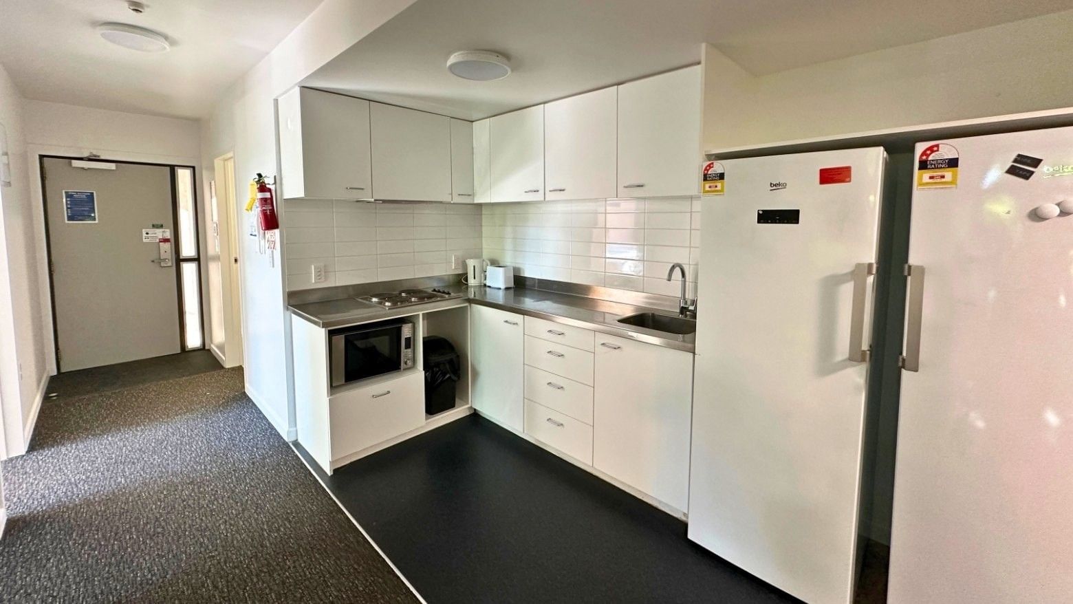 Modern kitchen area with white appliances and cabinets in student accommodation.