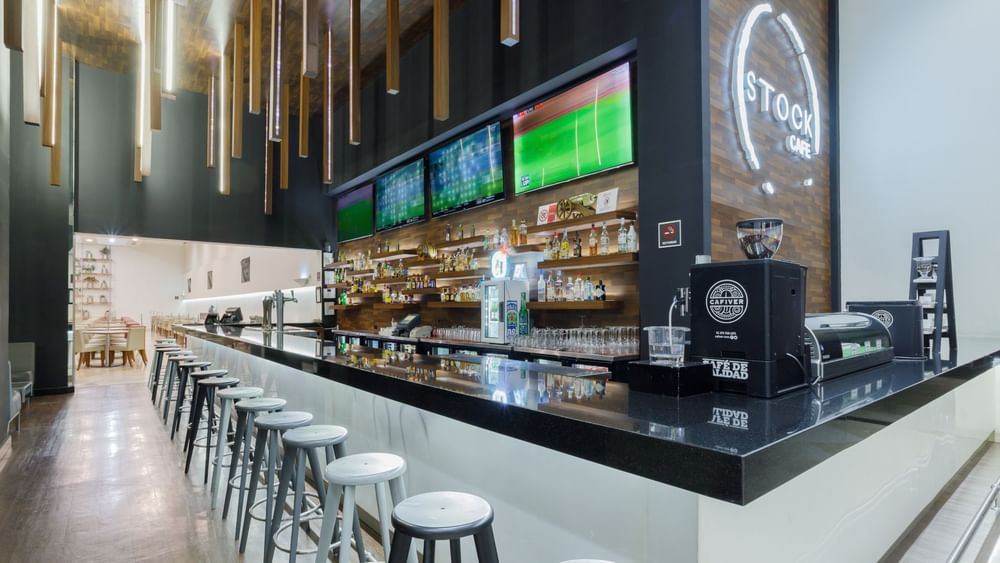 Stock Bar with black counters, high stools, and multiple TV screens at Real Inn Tijuana
