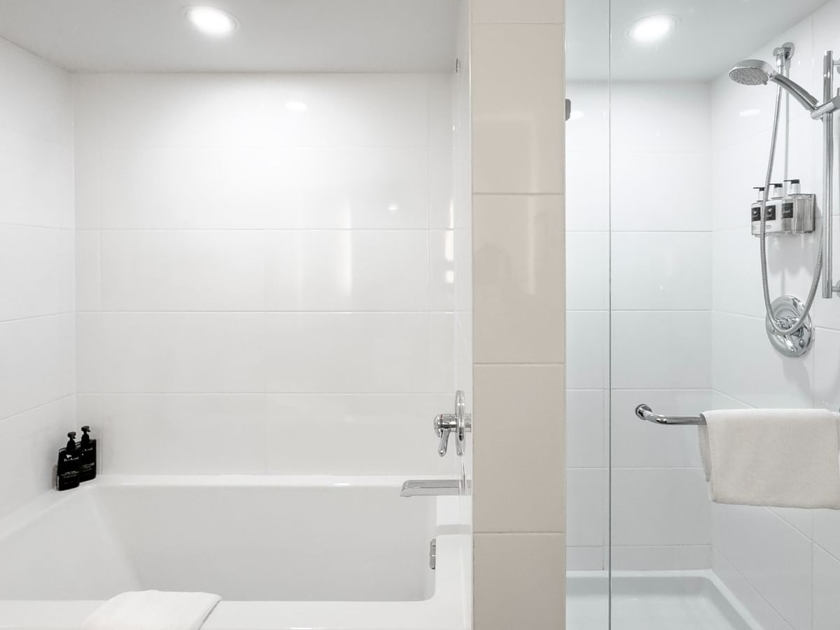 A bathroom with white tiles, a bathtub, a shower stall, and towels hanging on the side.