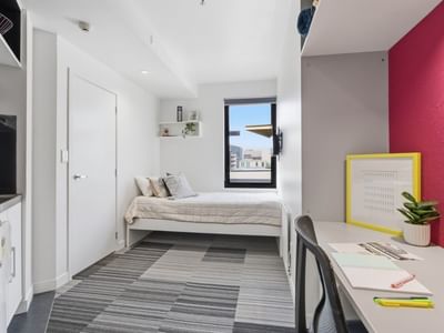 Compact room with bed, desk, and small kitchen area at UniLodge Auckland City.