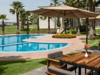 Sunny outdoor pool featuring wooden tables and blue poolside views near Camino Real Puebla Angelopolis