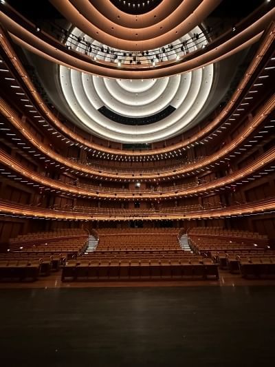Rows of theatre seating beneath arced balcony levels and circular lighting overhead. 