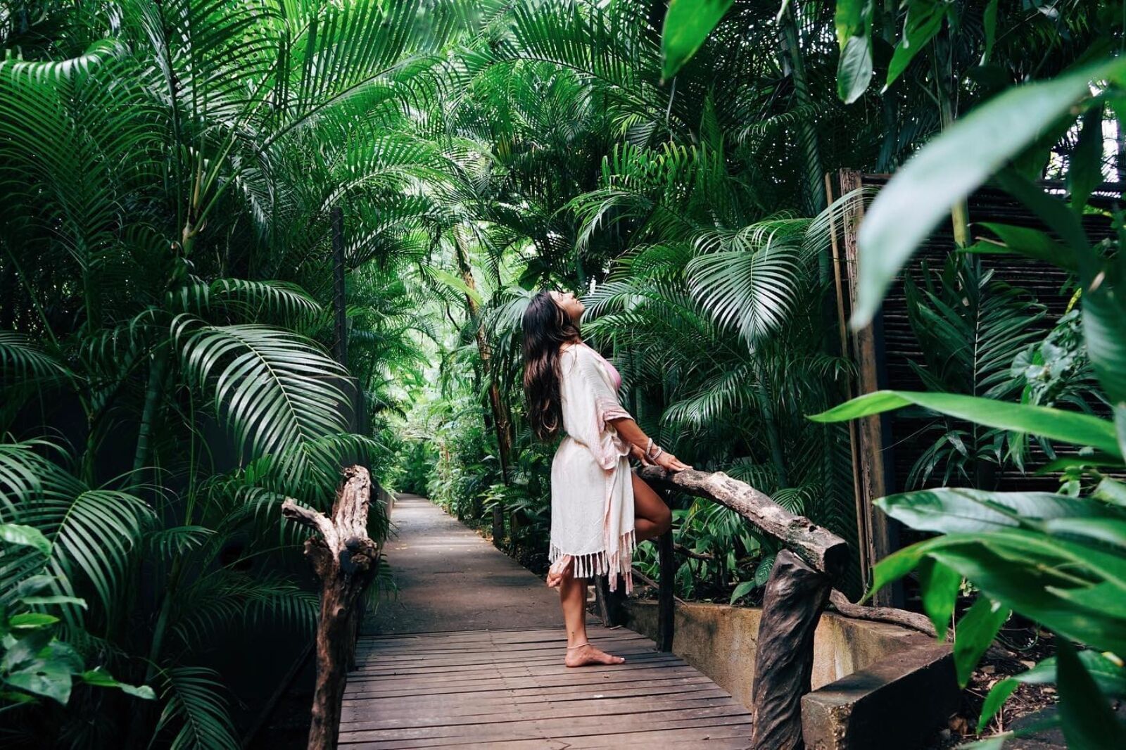 Woman walking a tropical wooden bridge surrounded by dense green palm leaves at Cala Luna Boutique Hotel