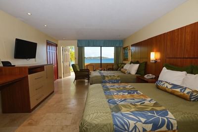 Two beds facing the TV on wood dresser beside open door with ocean views at the Lindbergh Bay Hotel & Villas