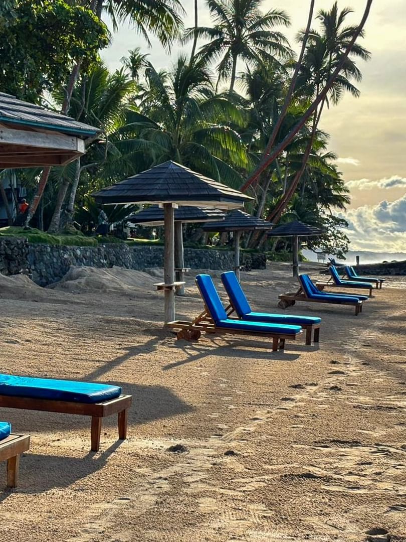 Blue lounge chairs on sand beach under umbrellas at Warwick Fiji Resort and Spa in Korolevu
