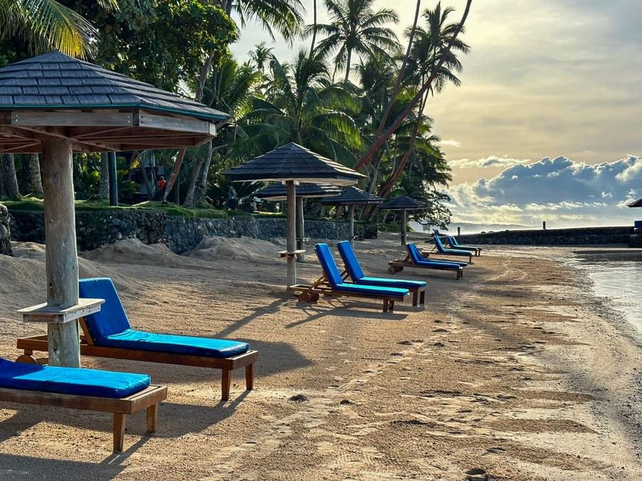 Blue lounge chairs on sand beach under umbrellas at Warwick Fiji Resort and Spa in Korolevu
