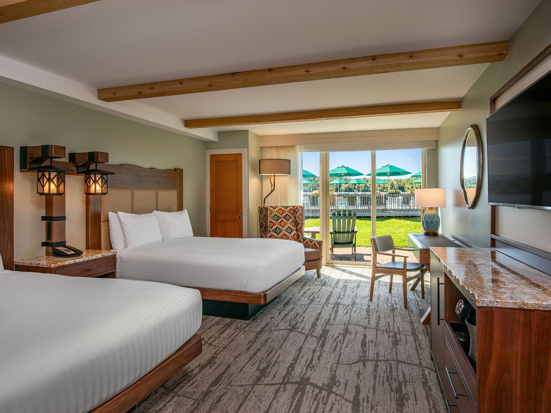 TV facing two beds with a couch by the window and a work desk in the Poolside King at High Peaks Resort