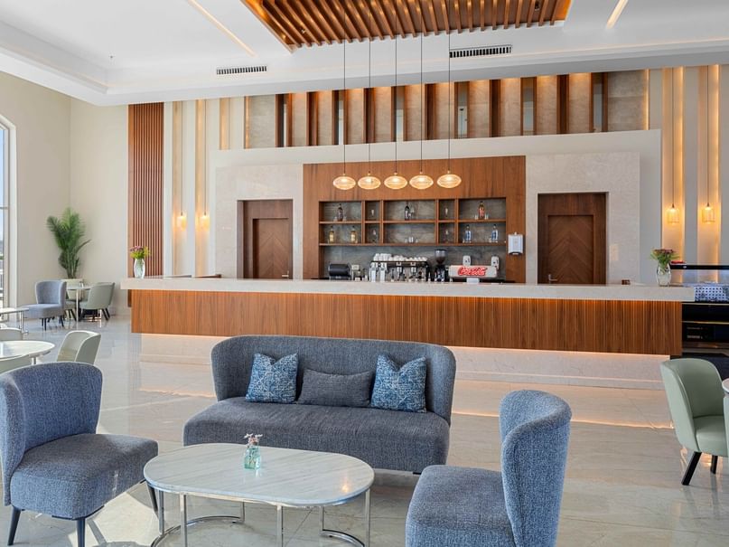 Modern lobby with seating, round table, and wooden reception counter with shelves and hanging lights above.