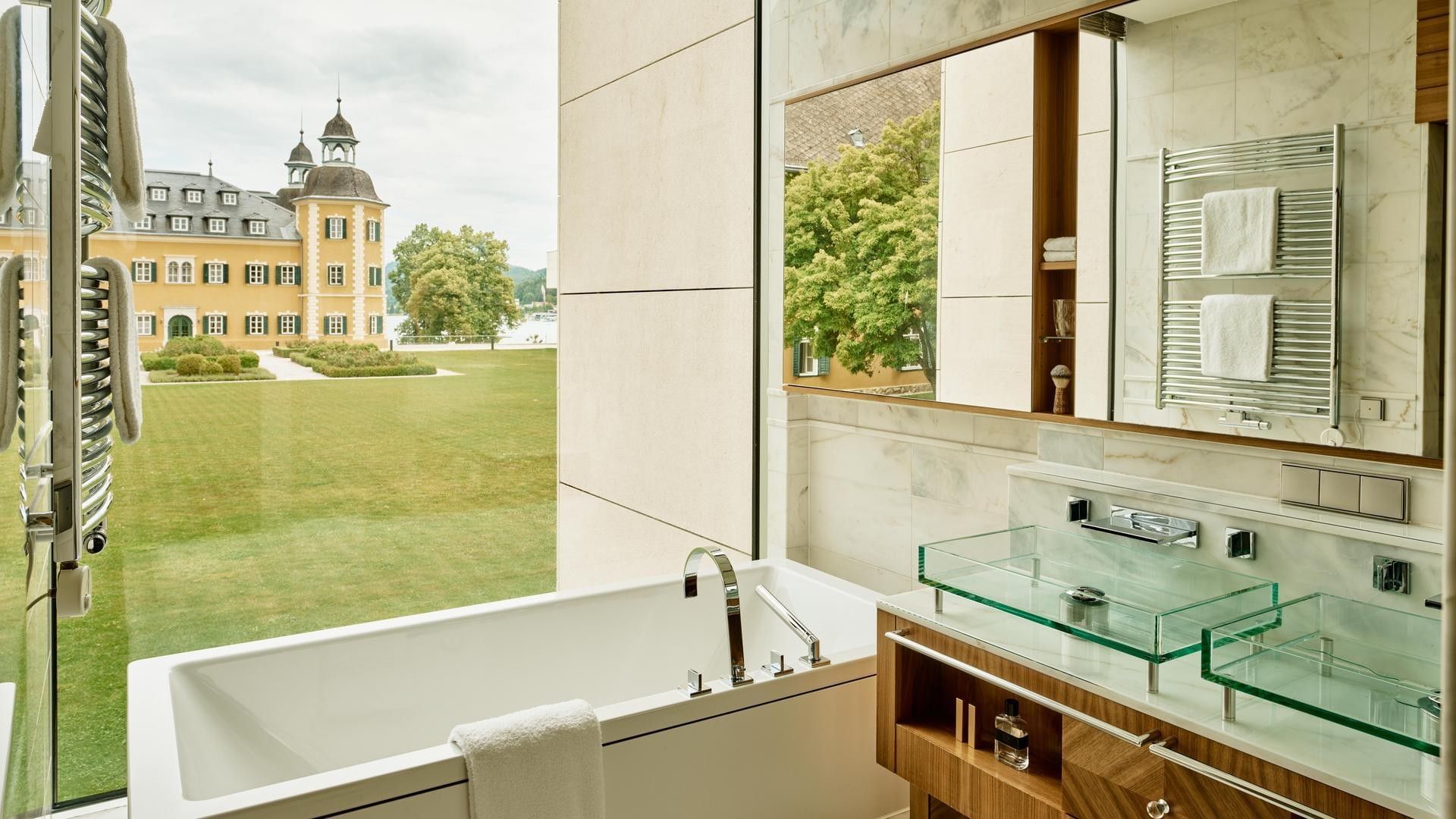 Large bathroom with a bathtub, glass sinks, and a window overlooking a green lawn.