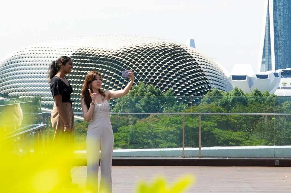 Two visitors taking a selfie on Esplanade Theatres on the Bay visible in the background near Grand Park City Hall