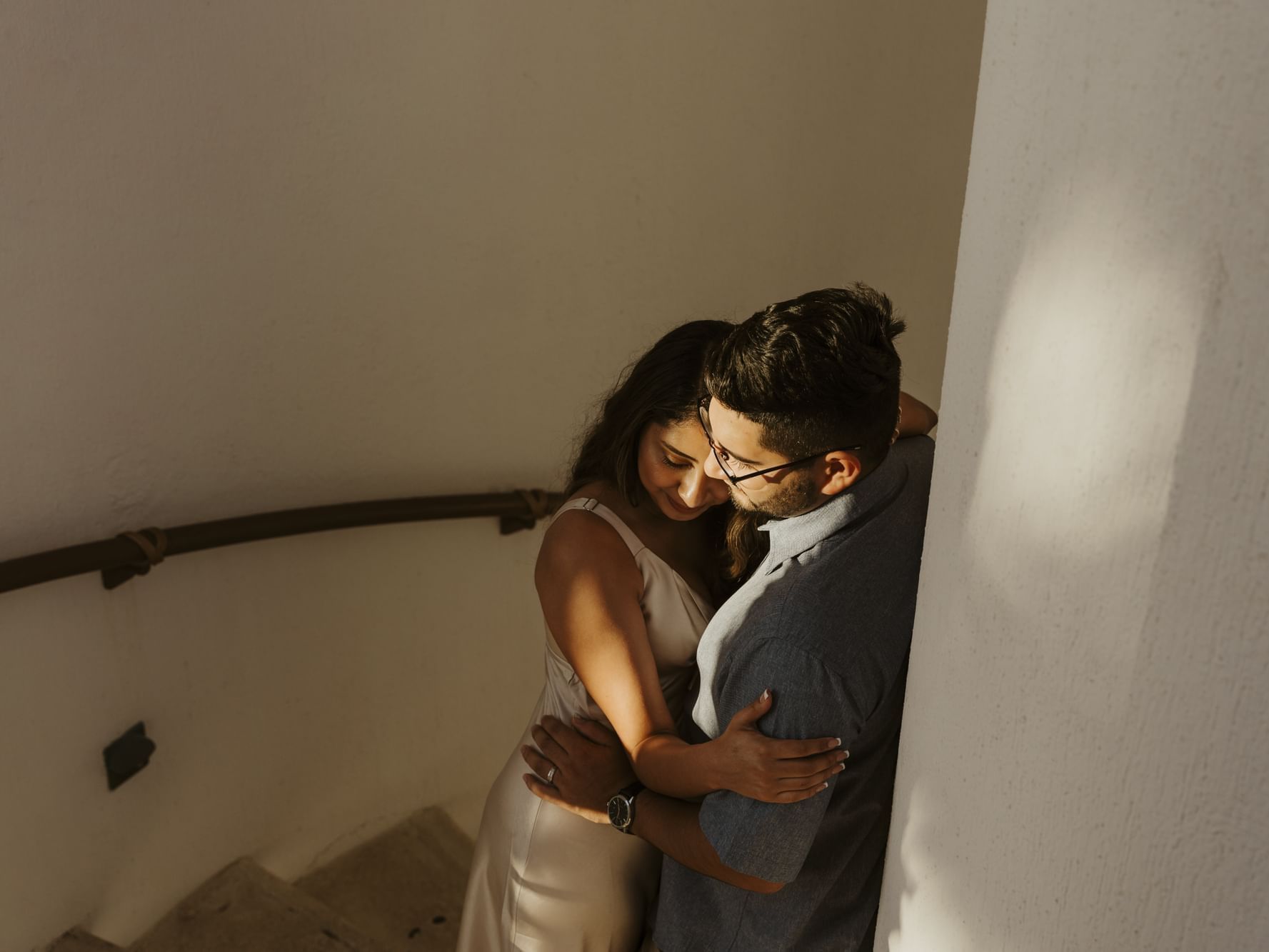 A loving couple embraces on a sunlit staircase, a tender moment captured at Marquis Los Cabos Resort
