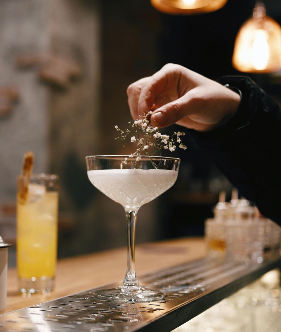 A hand garnishing a cocktail with tiny flowers in Regent Restaurant & Bar at Hotel Brookmere