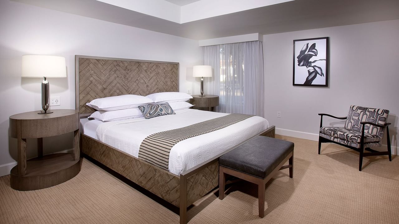 A cozy bedroom with a large bed, two nightstands, a chair, and a framed artwork on the wall.