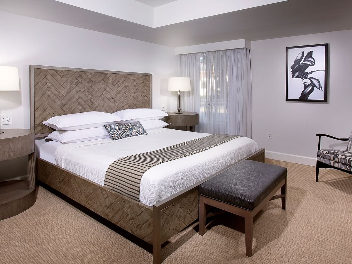 A hotel room with a bed, nightstands, lamps, armchair, artwork, and carpeted floor.