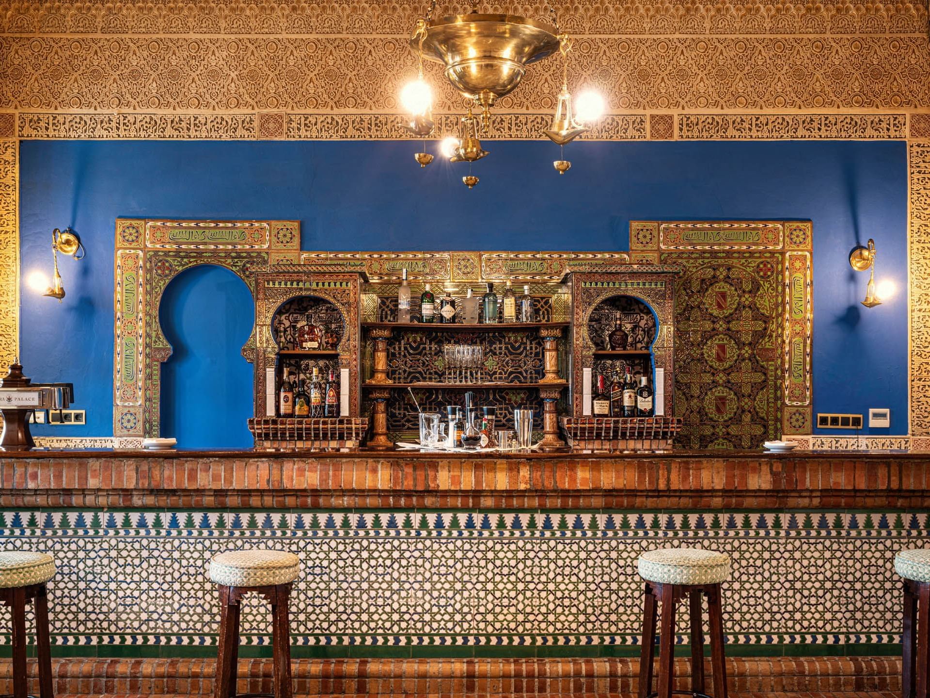 Bar Azul at Hotel Alhambra Palace with bright blue walls, Moroccan patterns, a wooden counter, and a display of liquor