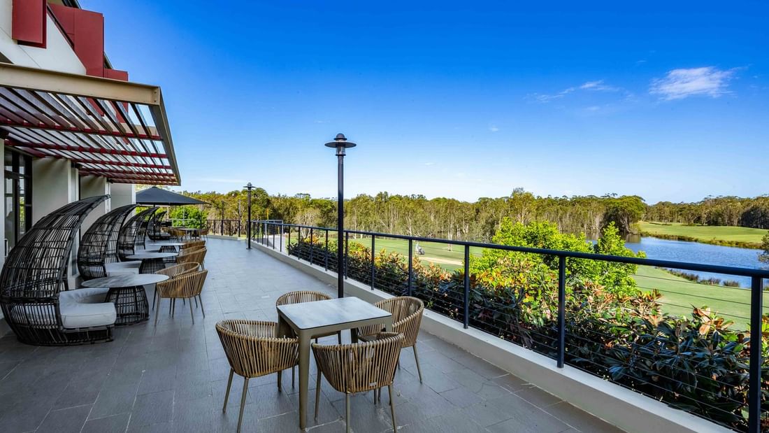 Terrace with tables and chairs, metal railing, and scenic view of a lake and golf course.