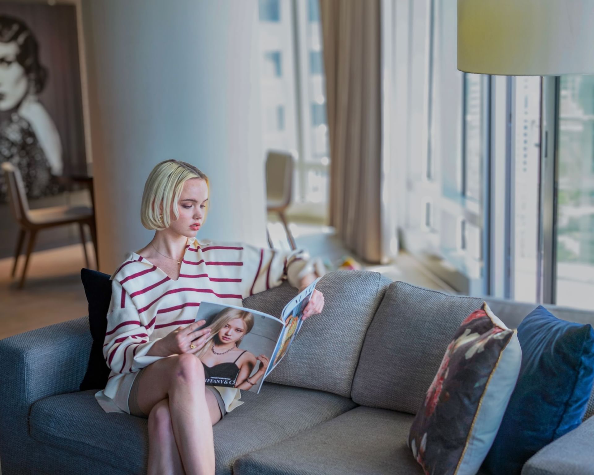 Paradox Vancouver Hotel guest reading a magazine on a couch near a large window with cityscape view.