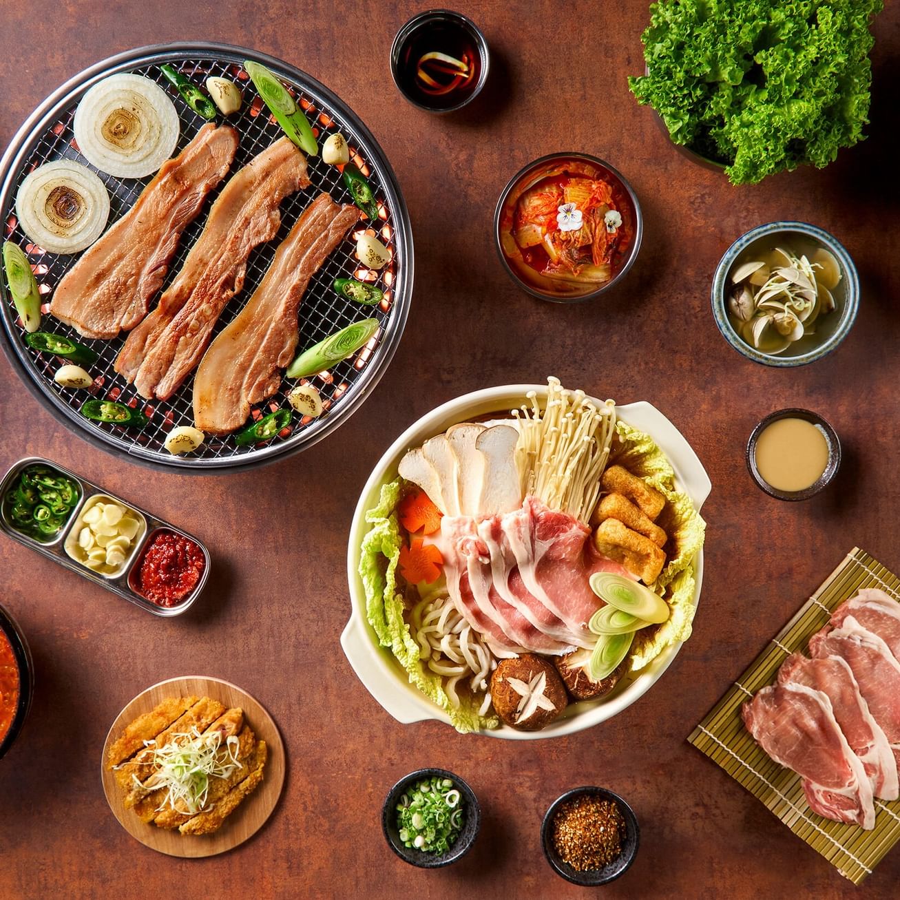 A variety of Korean dishes, including grilled meats, soups, and side dishes on a wooden table.