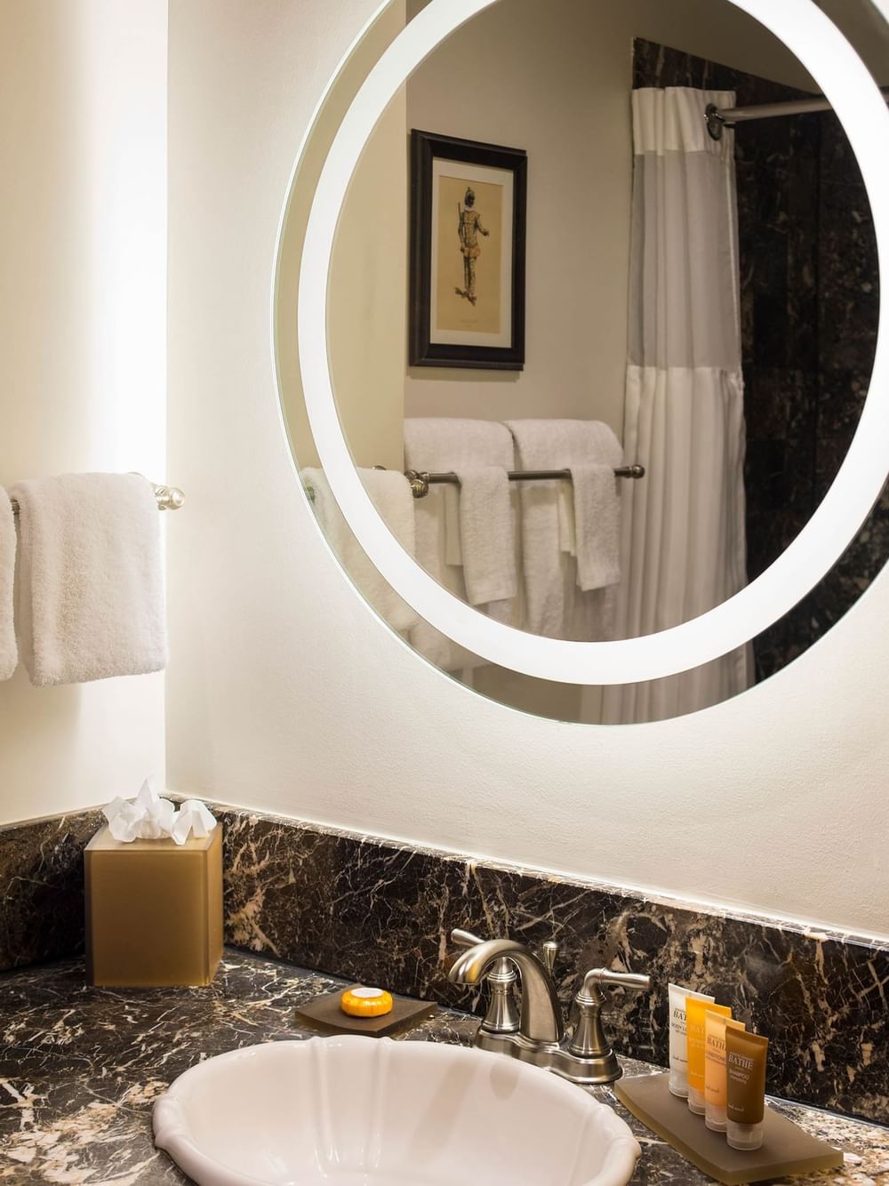 Round glowing mirror by white towels on a rack surrounding a marble vanity in Twin Room at Warwick San Francisco