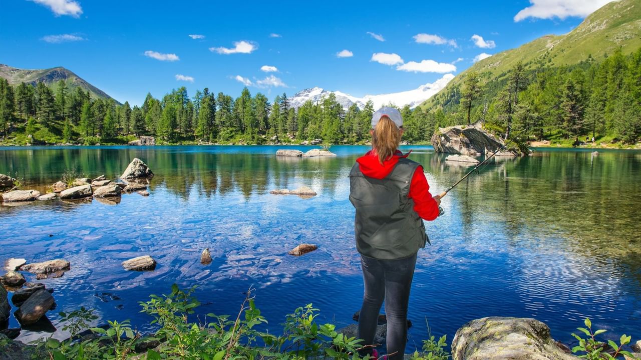 A person fishes on a blue lake in Canmore in the summer.