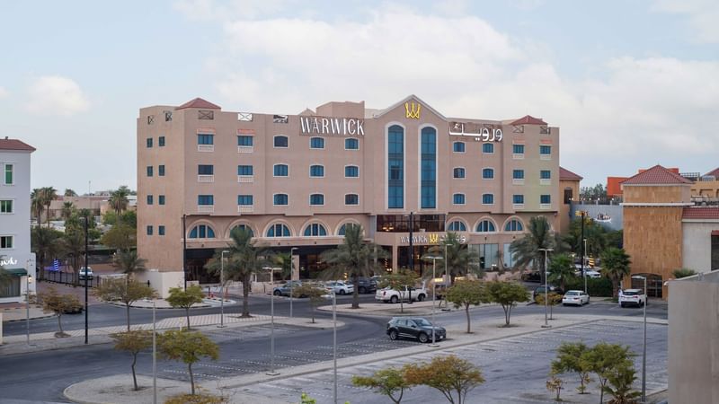 Warwick Hotel with several cars parked in front under a partly cloudy sky.